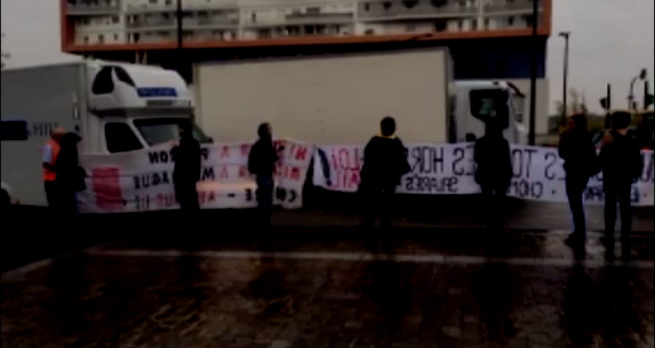 sieben Personen halten große Transparente und blockieren die Zufahrt von LKW