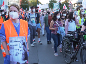 Demonstration von Krankenhausarbeiter_innen, eine Pflegerin im Vordergrund trägt ein Schild mit der Aufschrift: "Ich reanimiere deine Mutter"