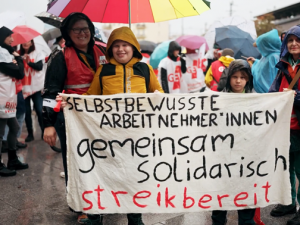 streikende Lehrerin mit Sohn halten Transparent "Selbstbewußte Arbeitnehmer*innen gemeinsam solidarisch streikbereit"