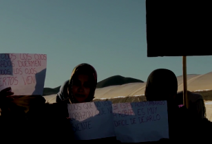 Sechs Frauen in einer Wüstenlandschaft halten Protestschilder hoch 